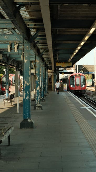A London underground train with a red and silver exterior is positioned at an outdoor station platform, ready for home relocation or furniture transport. The platform features tactile paving strips ne